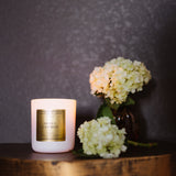 Candle with a gold label and flowers on a wooden surface against a dark background