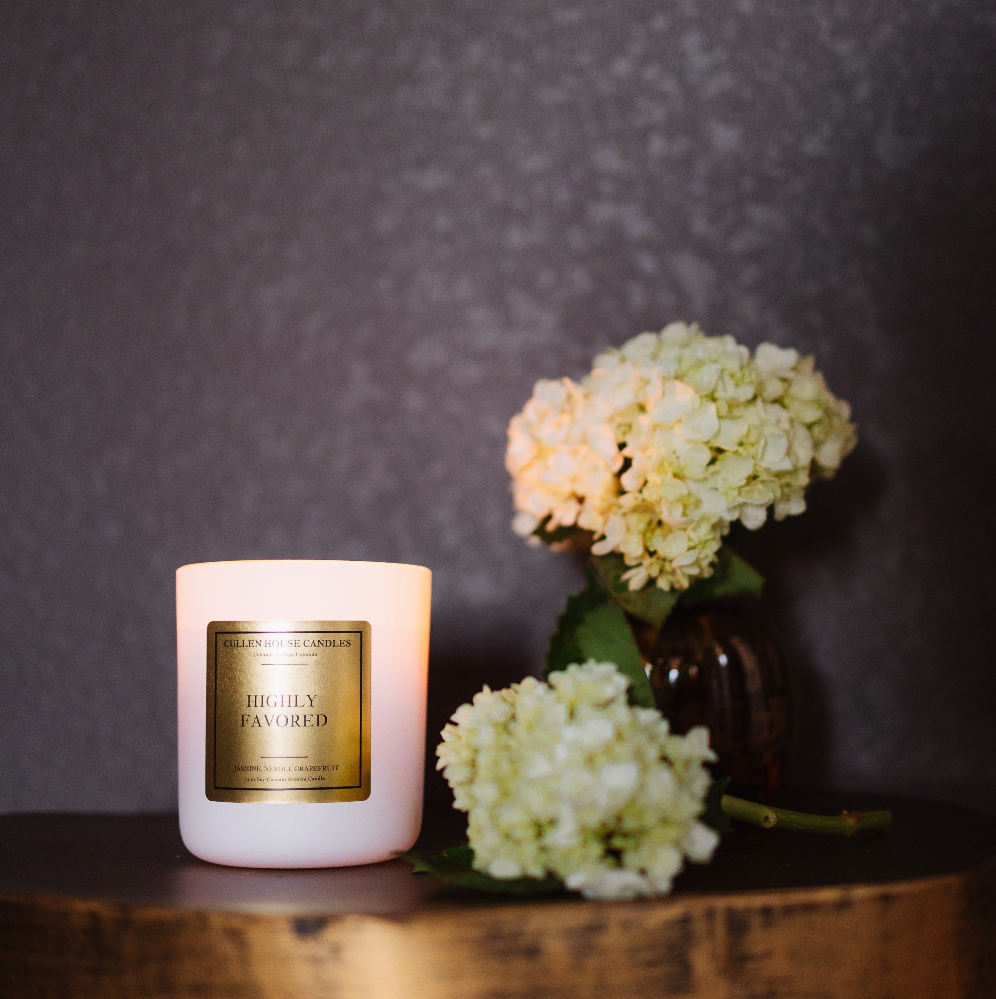 Candle with a gold label and flowers on a wooden surface against a dark background