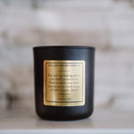Black candle with a gold label on a neutral background