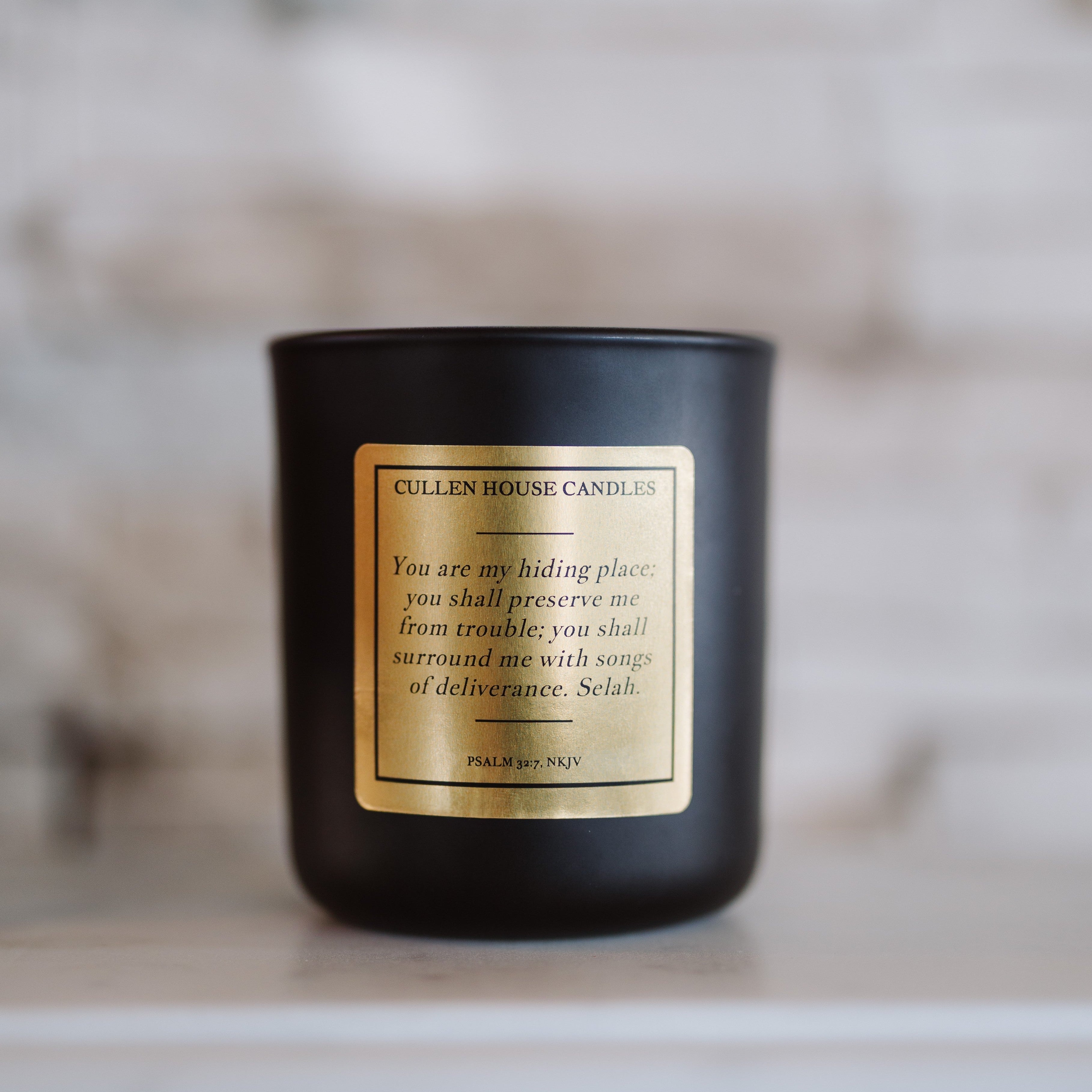 Black candle with a gold label on a neutral background