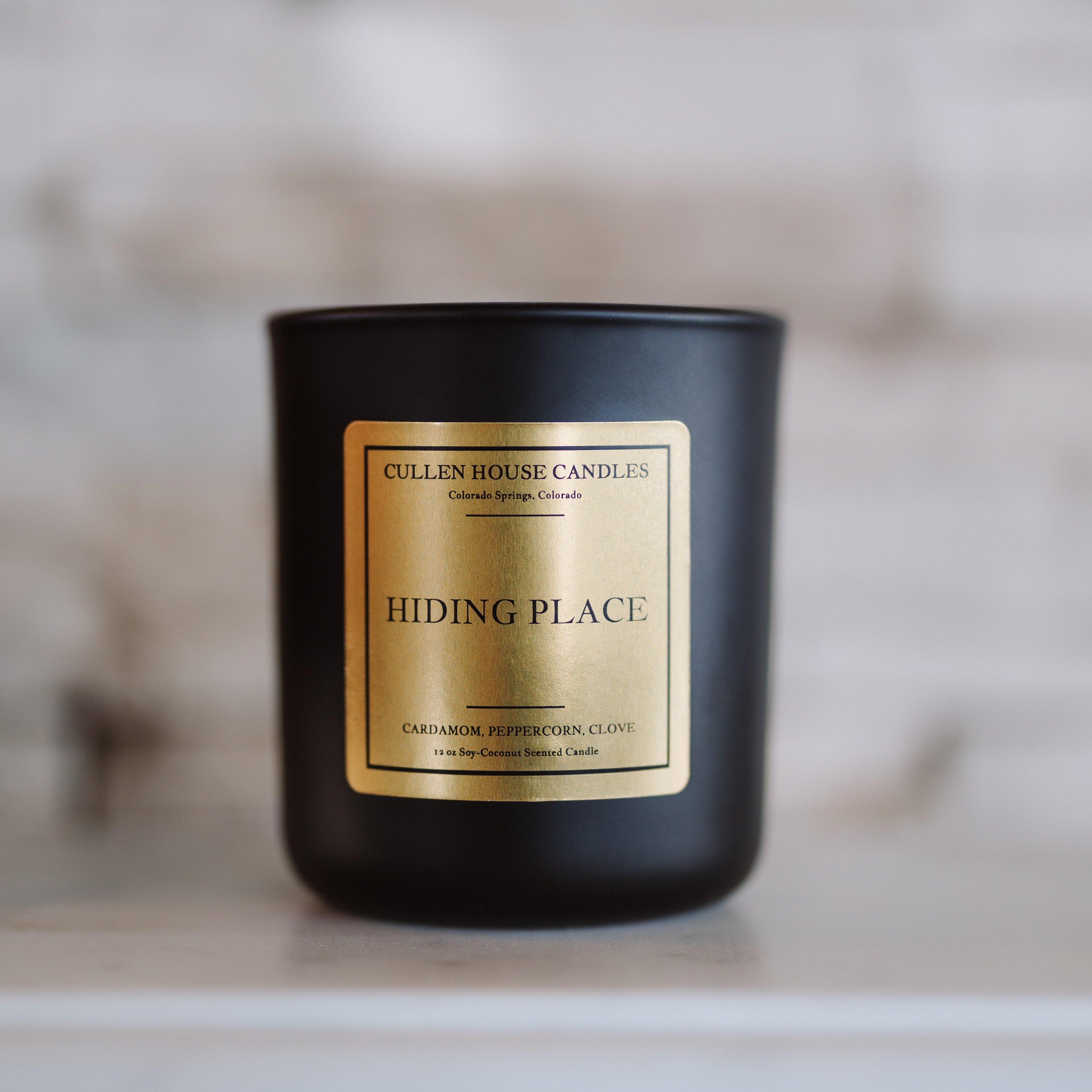 Black candle with a gold label on a white surface