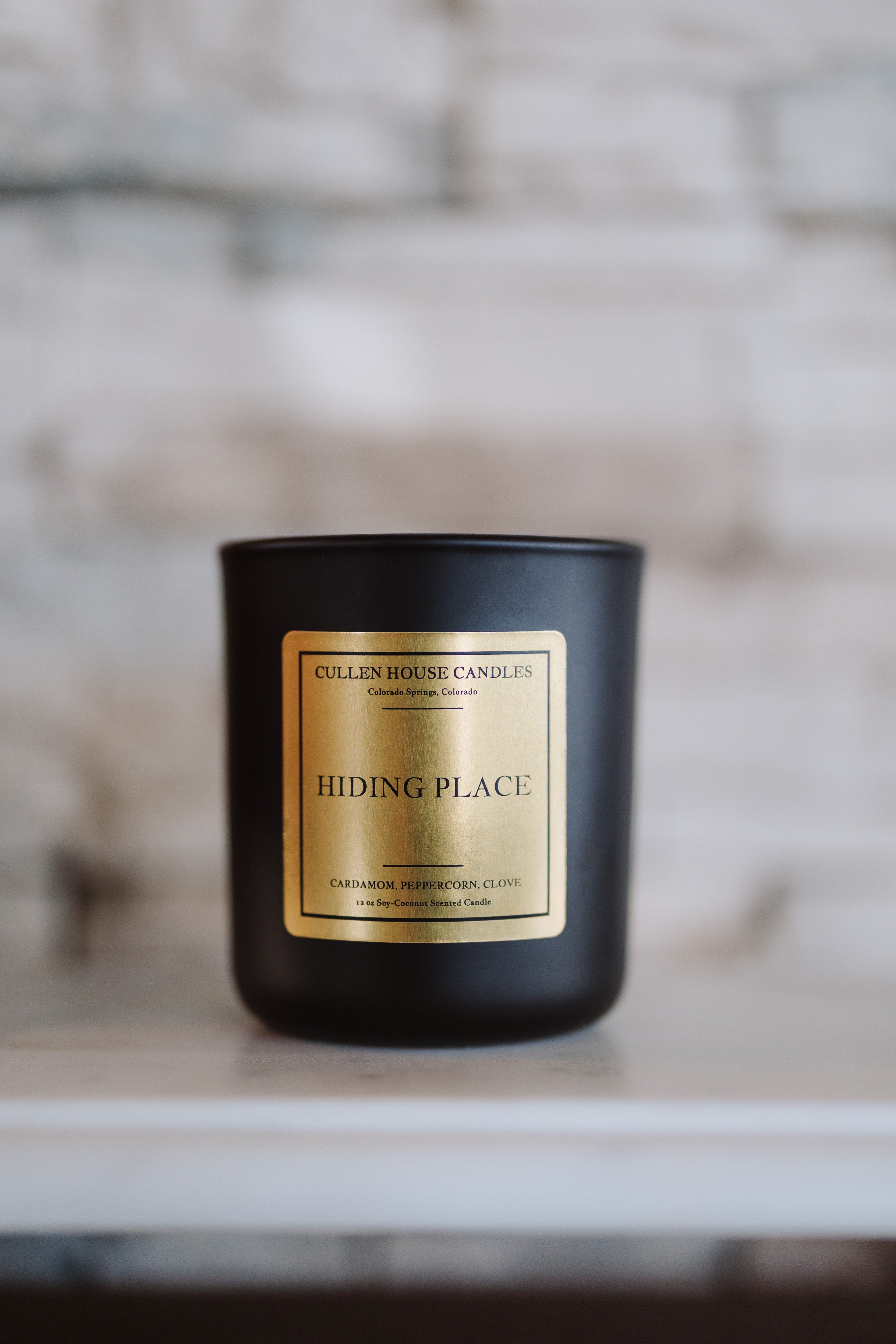 Black candle with a gold label on a white surface