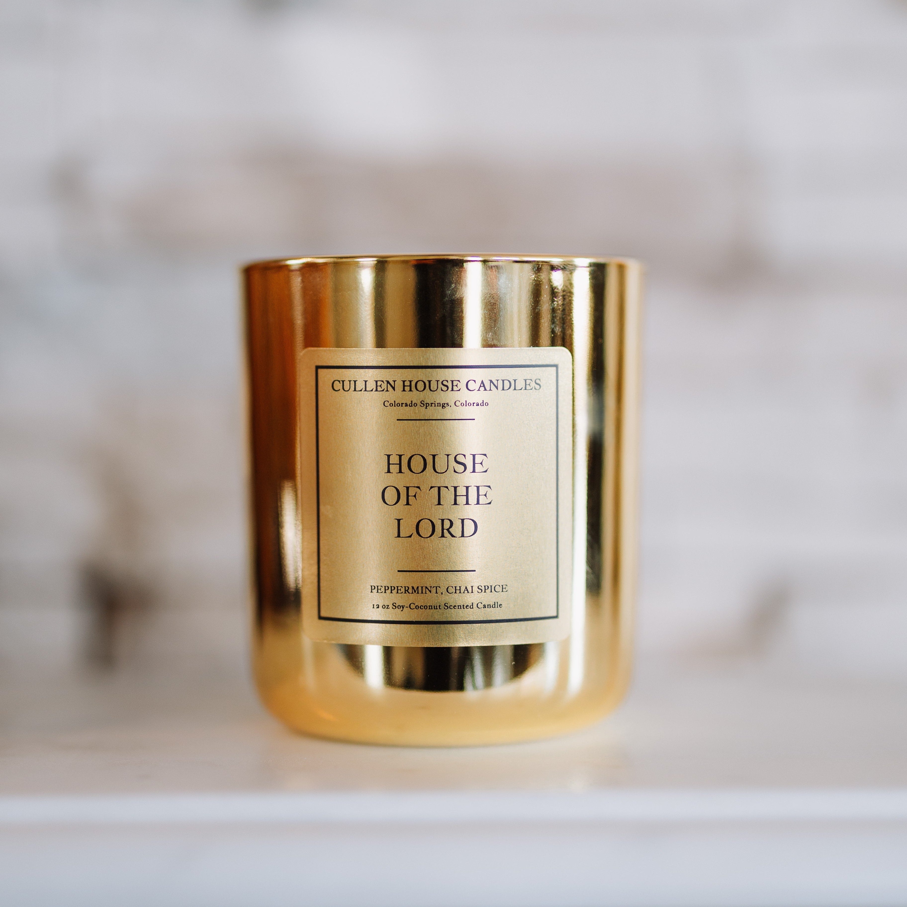 Gold candle with 'House of the Lord' label on a marble surface