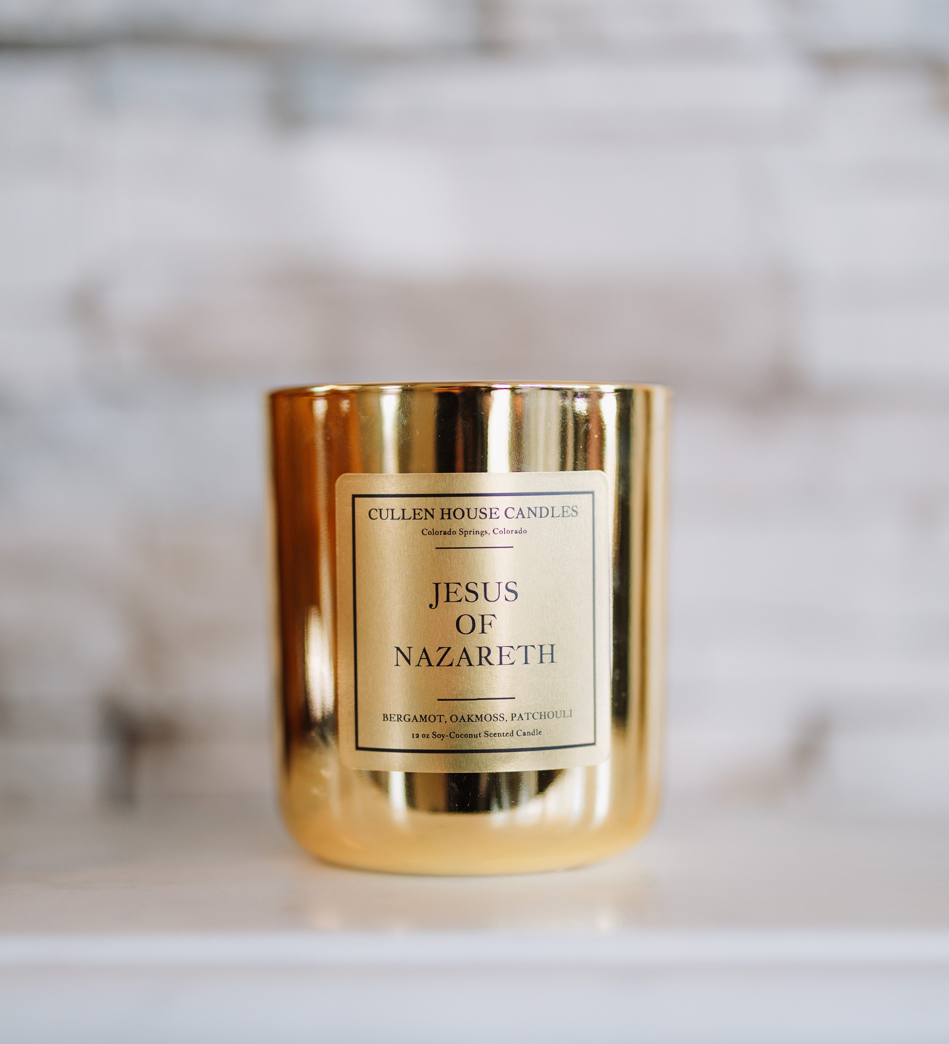 Gold candle with 'Jesus of Nazareth' label on a blurred background