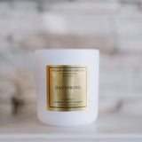 White candle with a gold label on a white surface with a blurred background