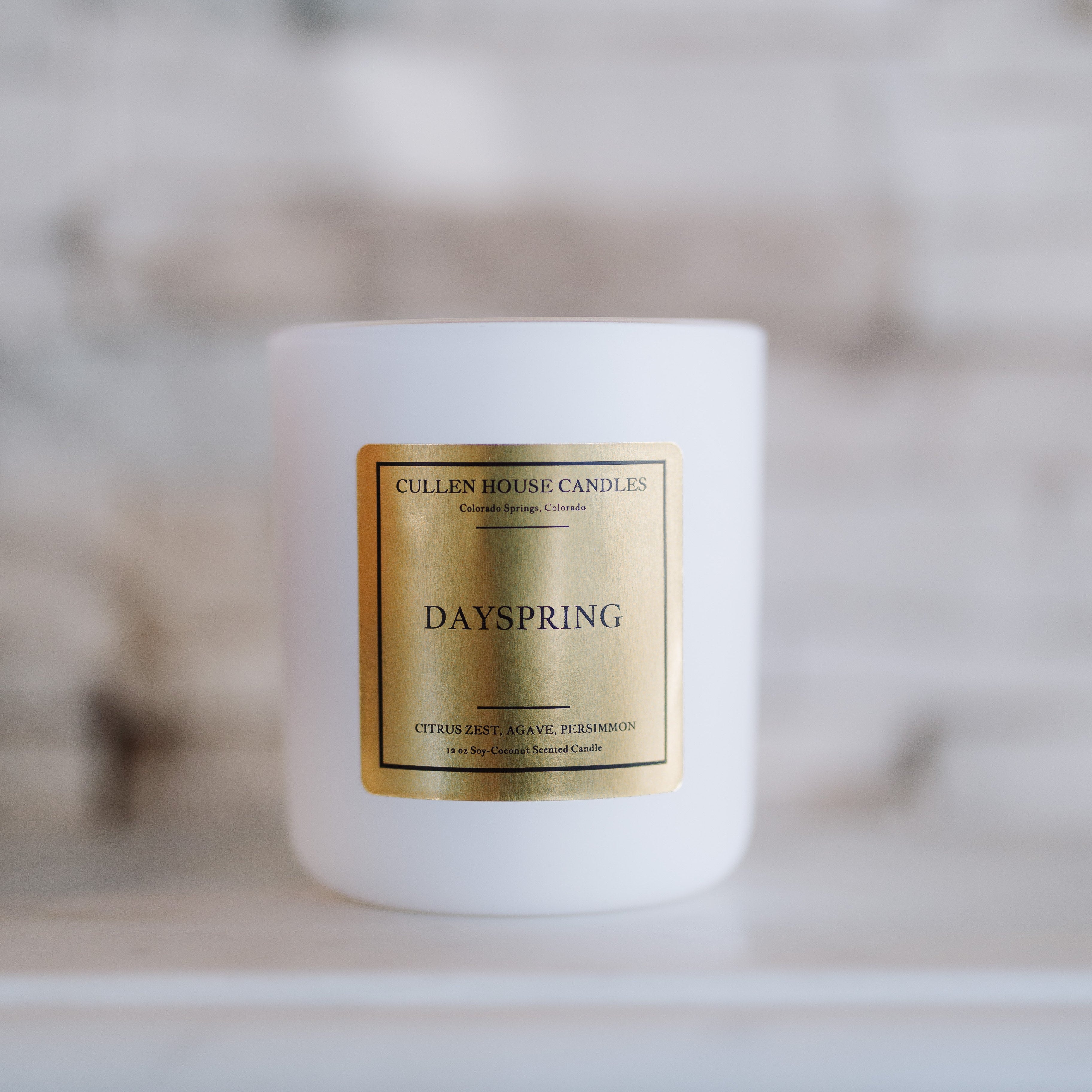 White candle with a gold label on a white surface with a blurred background