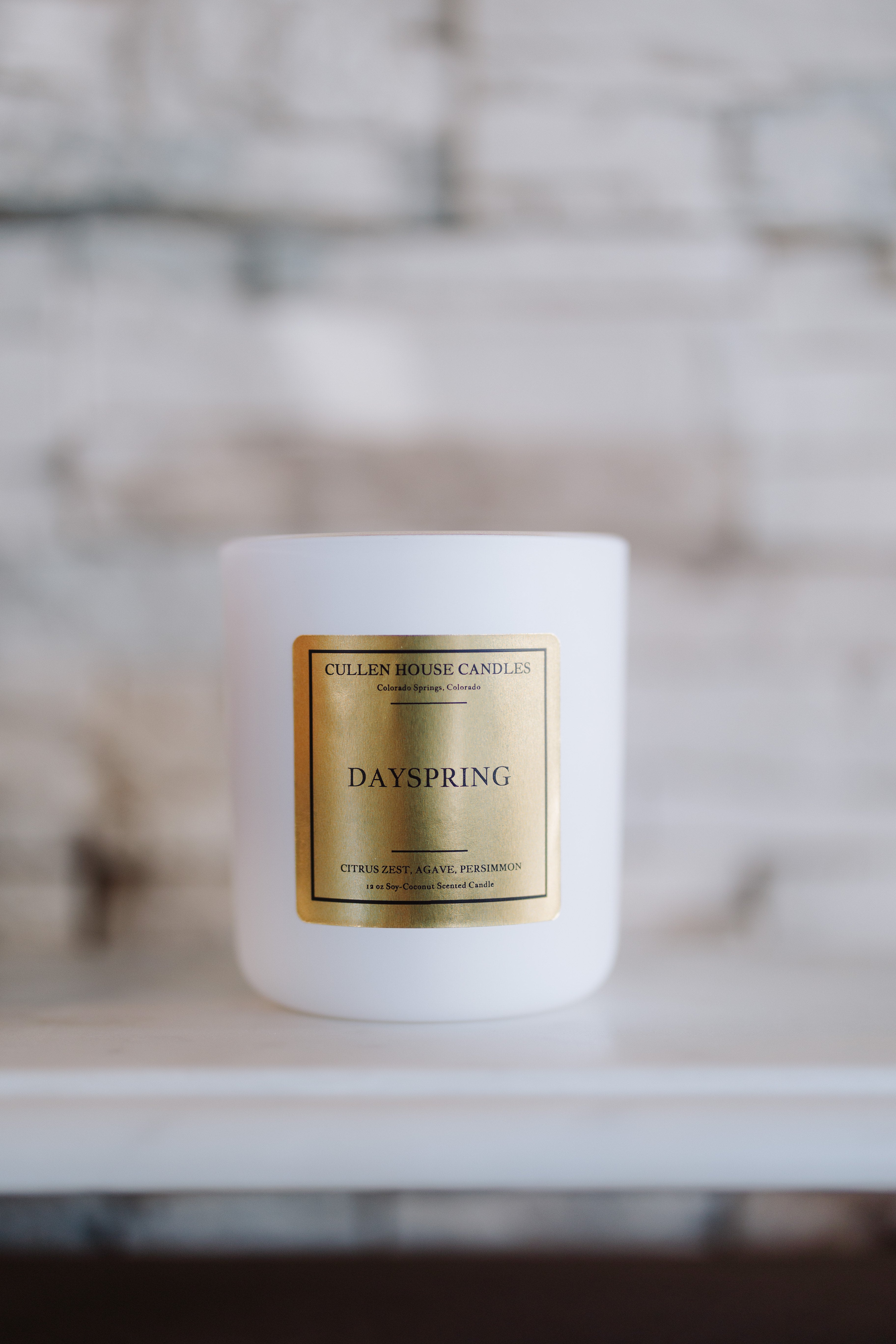 White candle with a gold label on a white surface with a blurred background
