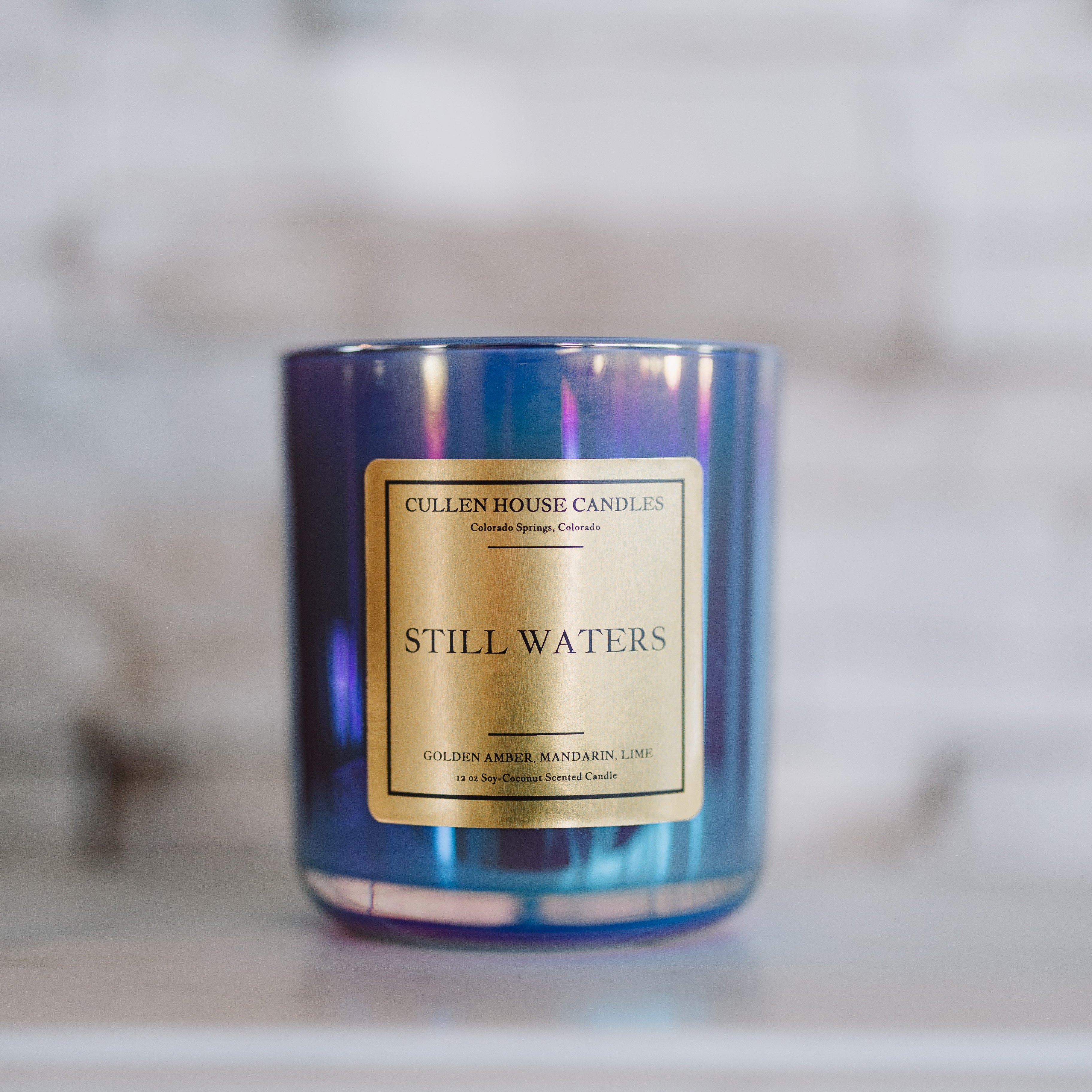 Candle with a blue tinge and gold label on a blurred background