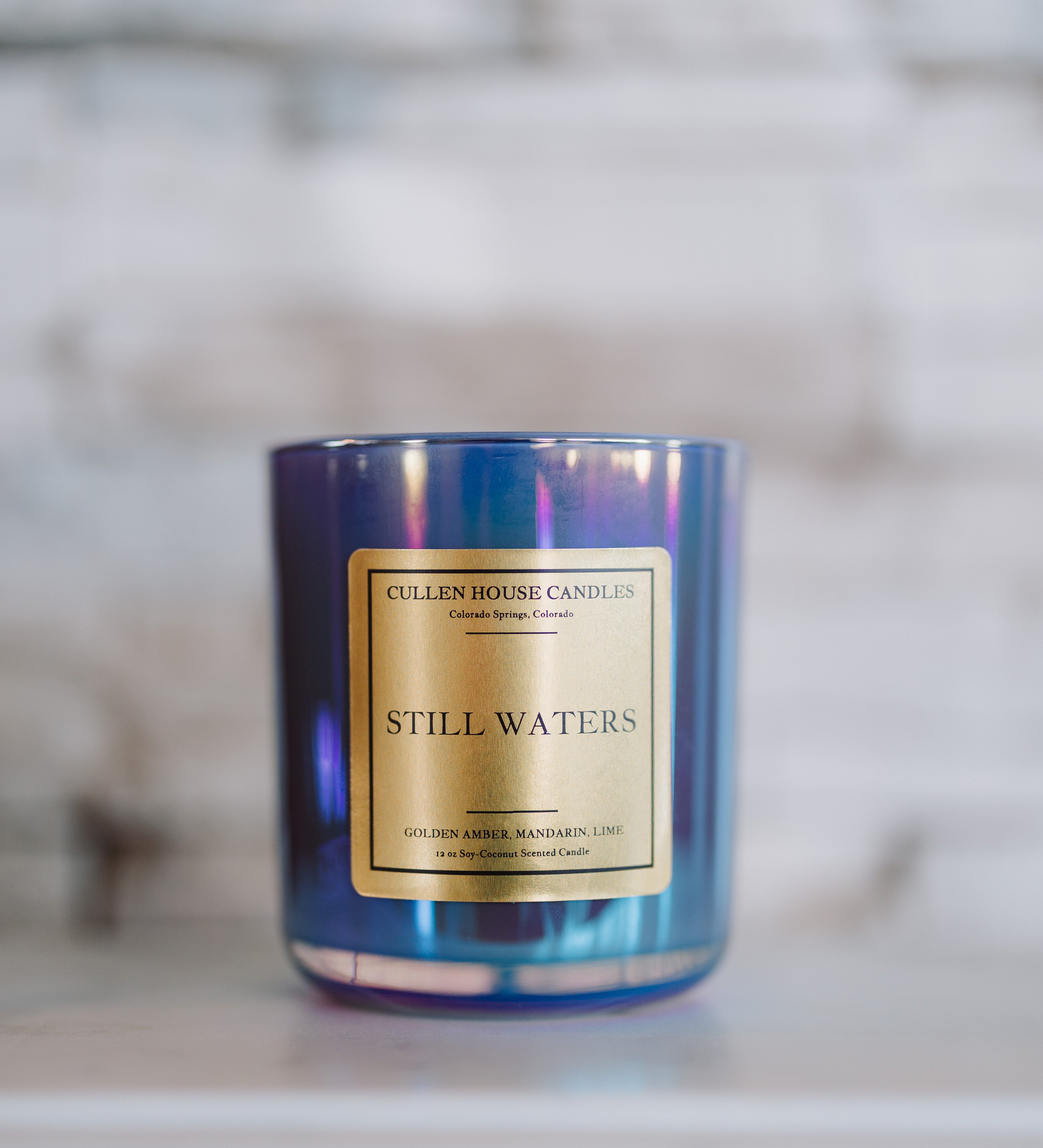 Candle with a blue tinge and gold label on a blurred background